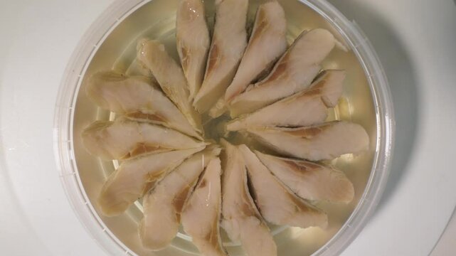 Fish in oil in plastic container, close-up. Top view. Herring fish macro shot. Slow motion