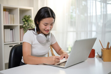 Asian high school student attending virtual class, taking notes and focusing on screen.