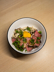 Rice bowl topped with beef slices, mushroom, and egg yolk.