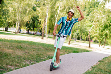 Young man in striped shirt enjoying a sunny day riding a scooter in the park © deagreez