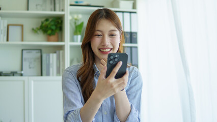 Smiling businesswoman checking messages on her smartphone while working at a modern office desk.