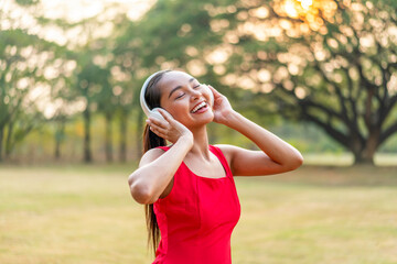 Naklejka premium Asian Woman in a Red Dress Dancing to the Rhythm While Listening to Music in the Park