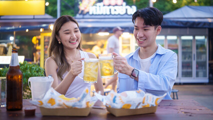 Happy couple toasting with beer at a vibrant street food market.