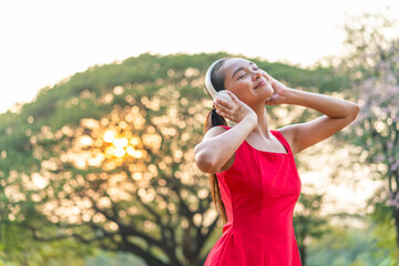 Obraz premium Asian Woman in a Red Dress Dancing to the Rhythm While Listening to Music in the Park