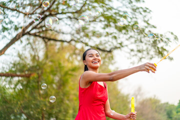 Happy Asian Woman in Red Dress Playing with Bubbles in Sunny Park