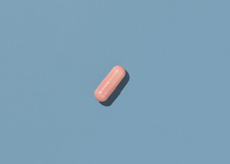 Pink Medical capsule on blue top view, hard shadows. Taking dietary supplements
