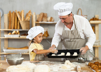 Father and little daughter put raw dough on baking sheet together to make croissants