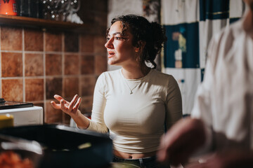 A woman stands in a warm, rustic kitchen, gesturing passionately while interacting with others.