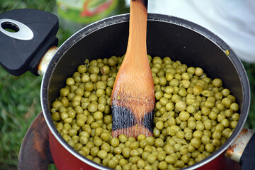 Green peas with a frying pan. Boiling green peas in a pot with a wooden spoon on the grass