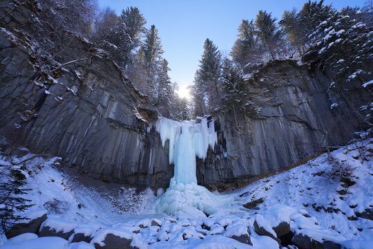 Majestic frozen waterfall in winter landscape with icy formation and snowy terrain under sunlight - Powered by Adobe