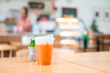 Ice Thai tea in clear plastic cup famous beverage drink traditional on wooden table in nature cafe, copy space