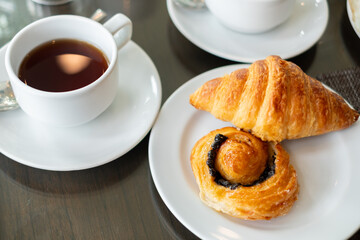 Freshly brewed tea served with croissant and pain aux raisins on white plates. A perfect continental breakfast setup for cafés, restaurants, or lifestyle food promotions