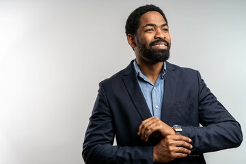 Black businessman adjusting his cufflink, smiling confidently. Wearing a suit with a watch on his wrist, isolated on a bright, elegant background.