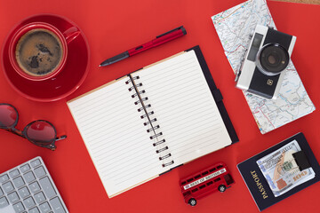 Travel planning essentials on vibrant red background. Flat lay with passport, notebook, camera, and coffee.