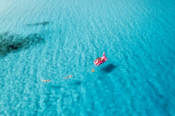 Aerial view of Inflatable pink flamingo with people on crystal clear blue water on summer sunny...