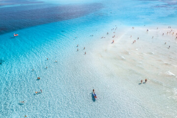 Aerial view of clear blue sea with swimming people. Top view from drone of beach with white sand, blue transparent water on sunny day. Summer in La Pelosa beach, Sardinia, Italy. Tropical landscape