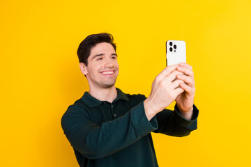 Young cheerful man in casual green polo shirt posing with smartphone against vibrant yellow background