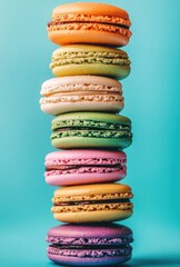 Colorful macaron tower against a teal background.  A delightful stack of various flavored macarons in vibrant colors, arranged vertically against a bright turquoise backdrop