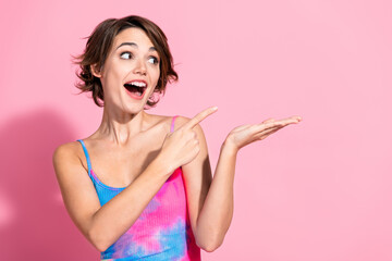 Charming woman in a colorful summer dress poses against a vibrant pink background, pointing and...