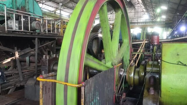 A green flywheel of a steam engine spins rapidly, converting piston motion into rotational energy, showcasing classic mechanical power in continuous motion.