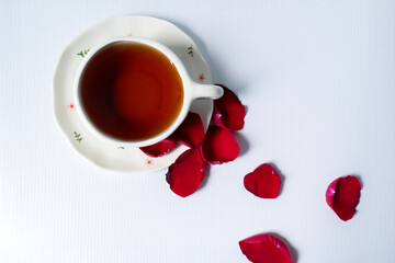 Top view of tea in cup with scattered rose petals. Perfect for romantic, cozy, morning ritual or floral tea content.