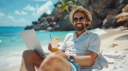 Fototapeta premium Young man holding a lapton and cool drink while sitting on the beach