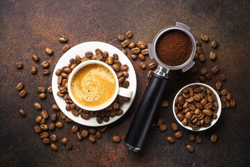 Cup of coffee, roasted coffee beans and filter holder at dark table.