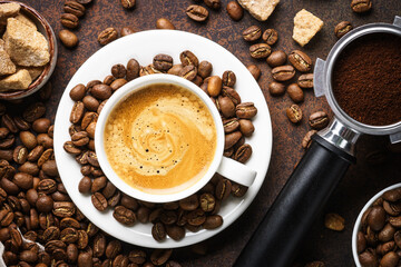 Cup of coffee, roasted coffee beans and filter holder at dark table.