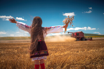 Young girl with traditional Bulgarian folklore costume at the agricultural wheat field during harvest time with industrial combine machine