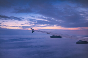 Airplane flying over color sky clouds during scenic sunset or sunrise cloudscape, view from plane window of wing turbines and horizon