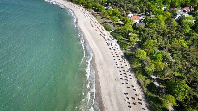 Aerial footage of the beach in Niendorf, a quiet part of Timmendorfer Strand, with beach chairs, wave breakers,  view of marina and curved coastline.
