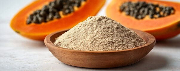 Dried papaya powder in wooden bowl, alongside halved papaya fruits