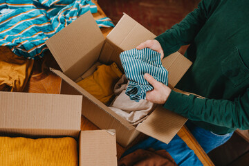 Unrecognizable man putting old clothes into box for charity or upcycling