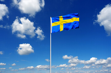 flag of sweden fluttering in the blue sky with cumulus clouds