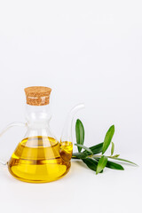 Transparent olive oil bottle and olive twig placed on white surface