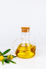 Olive oil in clear glass bottle with green olives and olive tree branches on white table