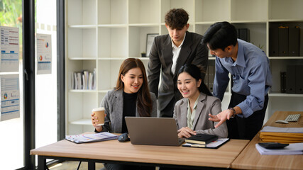 A Diverse young business professionals collaborating and reviewing content on a laptop in a modern office setting. Teamwork and positive communication in action