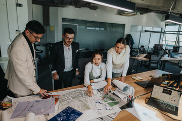 A group of people engaged in a project discussion, analyzing architectural plans in a modern office...