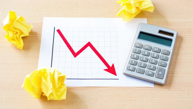 Financial graph with red downward arrow, calculator, and crumpled yellow paper, business loss, economic decline, financial challenges, budget cuts, profit decrease, cost reduction