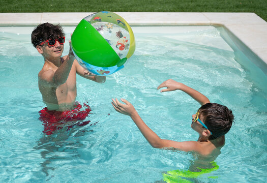 Two boys playing with inflatable beach ball in swimming pool