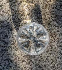 Top view of a clear plastic cropped bottle bottom with sparkling water on a granite surface.