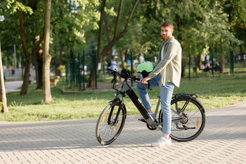Obraz premium Man riding an electric bike in a park during daytime while wearing a helmet and casual attire