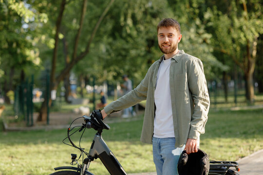 Young man enjoys a sunny day in the park while standing beside his bicycle - Powered by Adobe