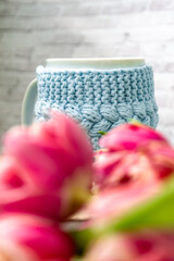 Pink tulips blurred foreground, open book and a mug of freshly brewed coffee or tea. Spring set