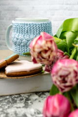 Pink tulips blurred foreground, open book and a mug of freshly brewed coffee or tea. Spring set