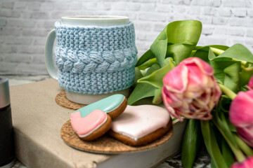 Pink tulips blurred foreground, open book and a mug of freshly brewed coffee or tea. Spring set