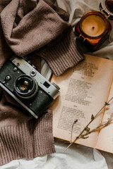 Vintage film camera with an old book wrapped in a warm knitted sweater and an extinguished candle next to it. View from above on a flat surface.
