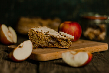 Traditional apple pie Charlotte apples are lying nearby. Sweet Thanksgiving dinner, autumn seasonal apple pie sliced one piece on wooden tray, on dark wooden background.