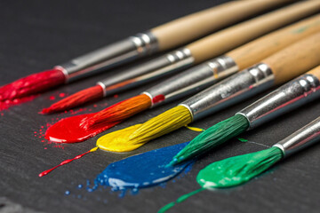 Fototapeta premium Against a dark artistic surface, paintbrushes with wooden handles display a vibrant array of colors through their textured brushstrokes.