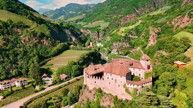 Flight around the beautiful medieval castle Runkelstein in Bolzano, South Tyrol, Italy. Amazing rocky landscape with vineyards growing on the slopes. Aerial view.